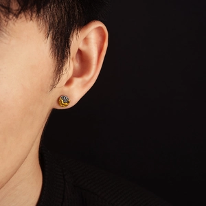 Detail of artistic gold and silver round stud earring featuring textured lava rock finish