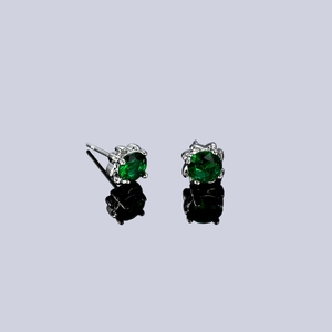 Detailed close-up of four-prong silver studs with emerald green cubic zirconia stones