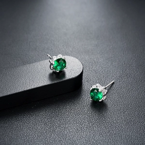 Macro shot of green zircon earrings with silver four-claw setting on black pedestal