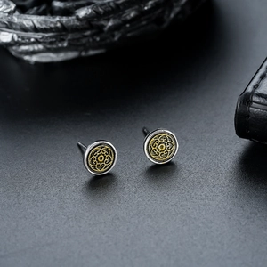 Macro shot of vintage round earrings featuring intricate gold totem patterns and silver frame