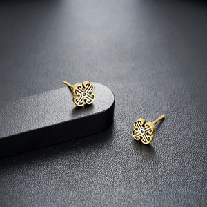 Golden four-leaf clover stud earrings with intricate cutout design on black display
