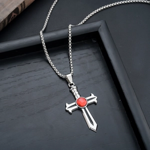 Close-up of a silver sword cross pendant with a red gemstone on a bead chain necklace