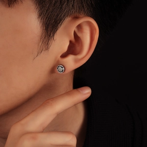 Close-up of retro silver sun-patterned round stud earring on ear with dark background