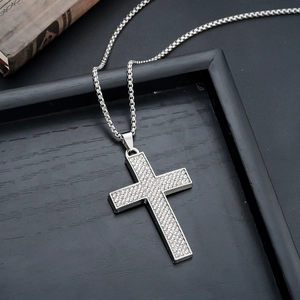 Close-up of a silver cross pendant with sparkling crystals on a black wooden tray
