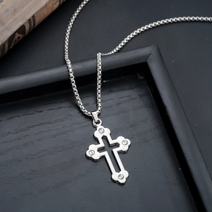 Detail showing a silver cross pendant with center rhinestone on a black wood tray