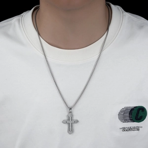Detail of silver cross pendant with cubic zirconia on box chain worn by a model