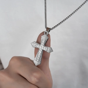 Close-up of silver cross pendant with inlaid crystals and textured edge on a steel chain