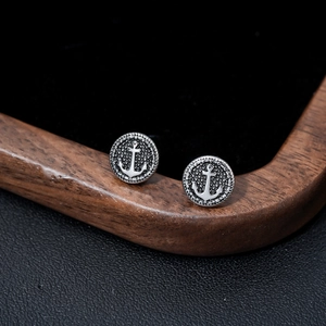 Close-up of vintage silver anchor stud earrings with round frames on a dark background