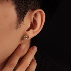 Close-up of a gold circular anchor stud earring with beaded edges on a male model