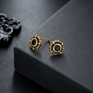 Macro shot of vintage gold starburst stud earrings featuring center green gemstones