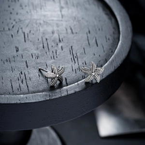 Macro shot of silver starfish stud earrings with vintage texture on dark wood stand