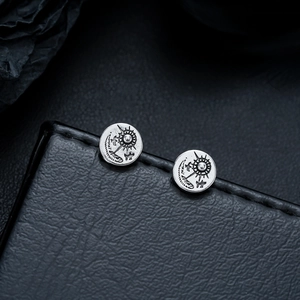 Macro shot of vintage round earrings with sun and moon engravings on black leather surface