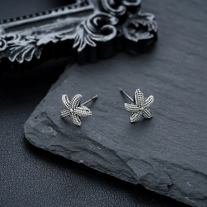 Macro shot of silver starfish studs with beaded texture on a grey stone background