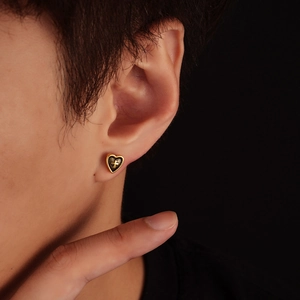 Golden heart stud earring with engraved cross on ear with black background