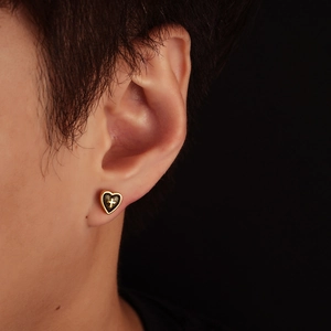Close-up of vintage heart stud earring with cross detail on model ear in black background