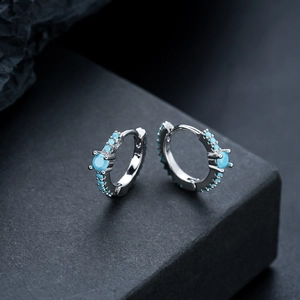 Silver-tone hoop earrings with turquoise stones on a minimalist dark textured surface