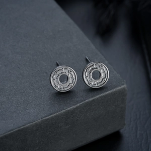 Polished silver and space gray coin-inspired stud earrings with embossed texture on a gift box