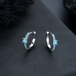 Macro detail of silver hoop earrings with turquoise stones on black leather and feather