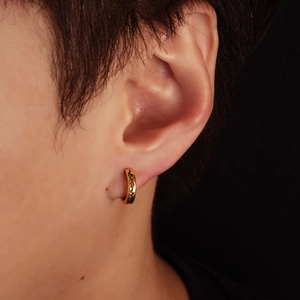 Close-up of golden textured hoop earring with wavy engraved pattern on male model