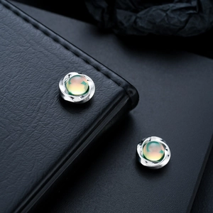 Macro detail of silver Mobius ear clips featuring opalescent cat eye stones on leather texture