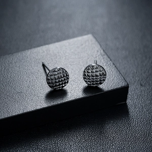 Macro shot of circular black stud earrings featuring a textured 3D prism pattern finish