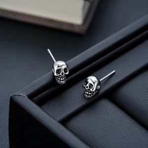 Macro shot of silver skull earrings with black eye sockets on black leather display