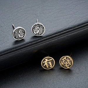 Detail view of retro matte earrings with embossed Chinese Fu characters in gold and silver