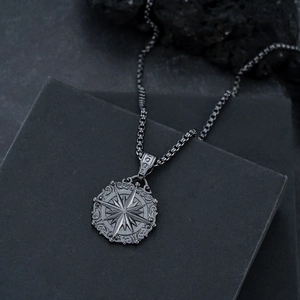 Vue détaillée du pendentif boussole noir avec gravure en étoile et chaîne à maillons carrés