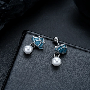 Macro shot of silver lotus stud earrings with blue enamel petals and round white pearls
