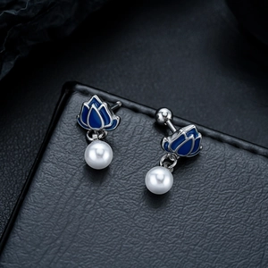 Detail of lotus earrings with blue enamel petals and white pearl drops on black leather