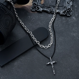 Detail of double-layered cross necklace with geometric black pendant on rock surface