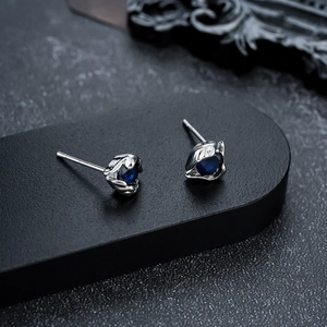 Detail of silver stud earrings with teardrop blue stones on a black textured background