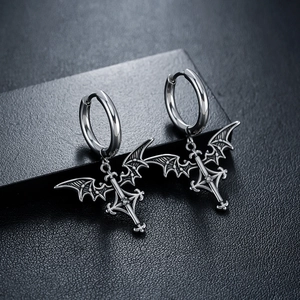 Macro shot of silver gothic earrings featuring bat wings, a cross, and a white zircon