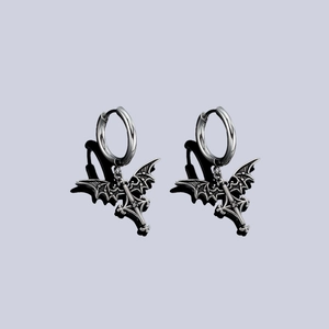 Gothic silver bat wings and cross drop earrings with punk aesthetic on a light gray background