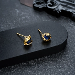 Detailed macro view of golden eye stud earrings featuring a blue oval gemstone setting