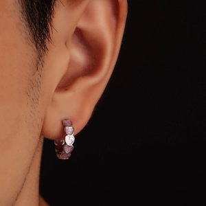 Gros plan d'une créole en cœur en métal argenté avec émail rose sur le lobe d'oreille