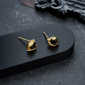 Close-up of gold eye stud earrings with round black stones on a dark display