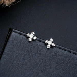 Macro shot of silver flower earrings with moonstone and textured rock finish on black leather