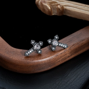 Macro shot of gothic cross heart earrings with clear zircon stones on dark wood
