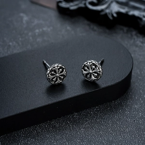 Close-up of vintage style round stud earrings with embossed cross pattern on a black stand