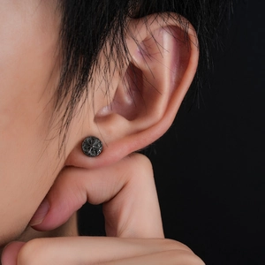 Macro shot of a vintage black cross stud earring with gothic floral relief texture