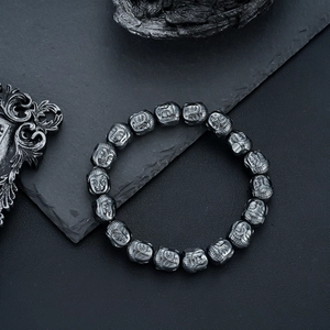 Men's gunmetal Buddha head hematite beaded bracelet on a dark textured stone background
