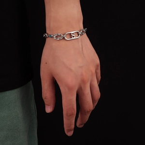 Bracelet en acier titane avec perles bleues et pendentif gravé S porté au poignet