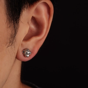 Detailed close-up of a vintage silver monkey head stud earring on a male model's ear