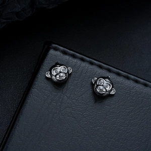 Macro view of gunmetal monkey stud earrings with detailed engraving on black leather