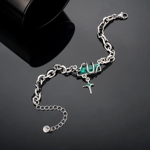 Detail of snake-style chain bracelet featuring a green crystal and silver cross pendant