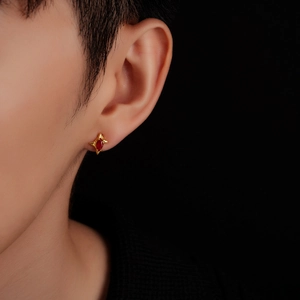 Detail of star-shaped gold stud earring with marquise red gemstone on ear