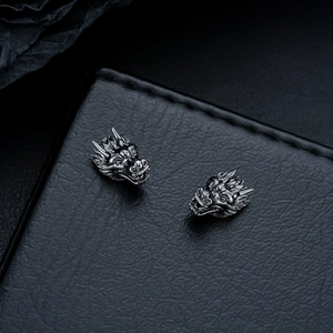 Detailed macro view of dark metal dragon head stud earrings on black leather surface
