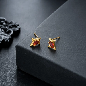 Close-up of star-shaped gold earrings with marquise-cut red zircon stones on a black box