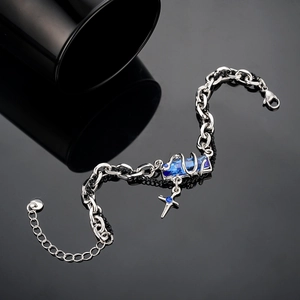 Detail of silver snake chain bracelet with blue crystal and cross pendant on black surface